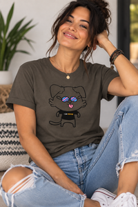 A woman wearing a dark olive brown graphic t-shirt with a cartoon dog wearing blue sunglasses and a black shirt that says 'I AM ENOUGH'. She is sitting in a brightly lit room wearing light-wash ripped jeans.